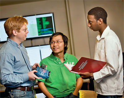 Tong Pham ’13 (center), electrical and computer engineering major, Kumera Bekele ’13 (right), computer science major, and Matthew Taylor, assistant professor of computer science, discuss the use of a scribbler robot in their research on the coordination of autonomous computer programs among themselves, which could have medical applications.
