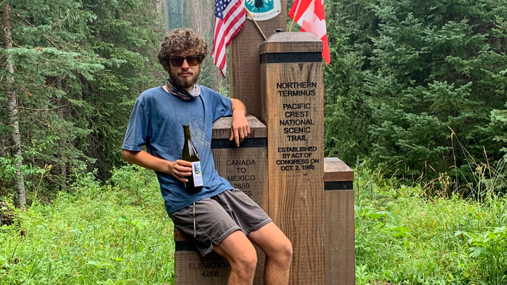 Ben Shmaruk with a full beard, visible weight loss at the northernmost trail marker of the Pacific Crest Trail