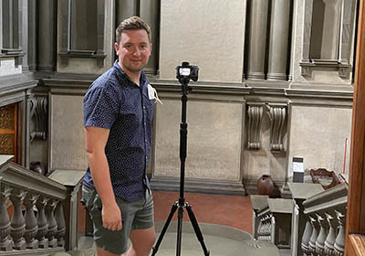 Eric Hupe stands near a camera on a tripod in a museum