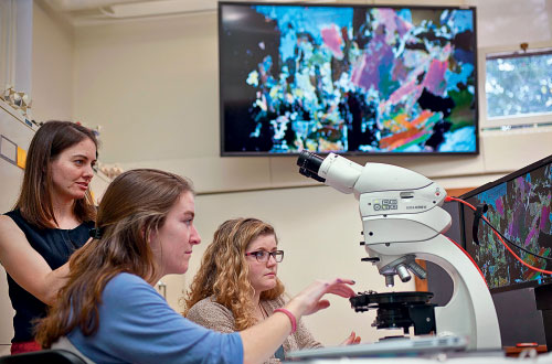 Tamara Carley, assistant professor of geology and geosciences (left) assists students Annika Leiby '18, (center) and Lissie Connors '18, with identifying a sample using the new high-tech lab with petrographic microscopes in Van Wickle Hall. 