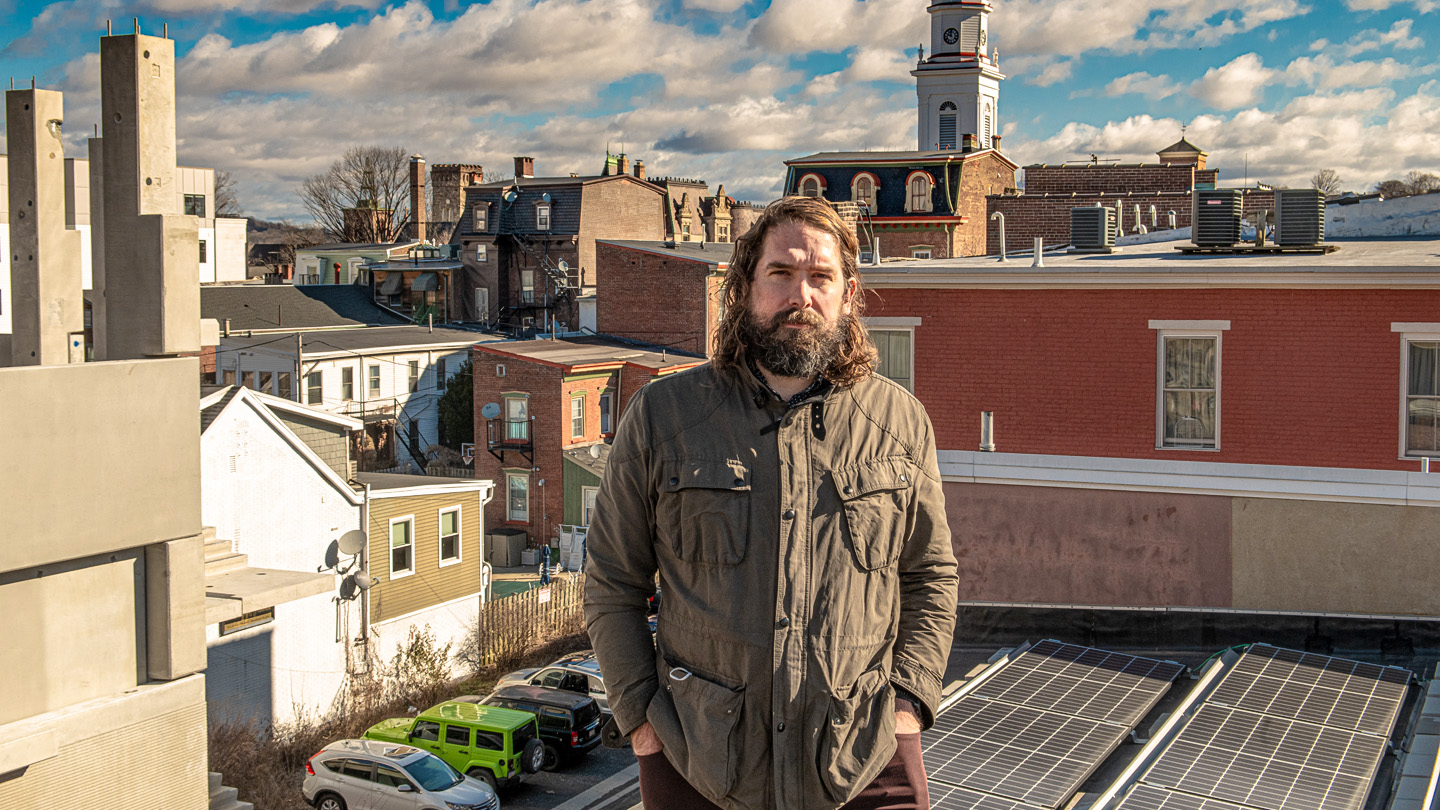 Jared Mast stands on a roof top with a solar panel and views of downtown Easton