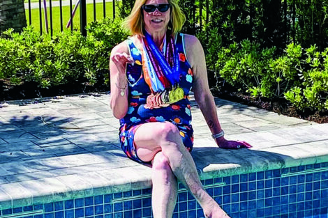 Margi Bergamini sits on the edge of a pool with medals around her neck