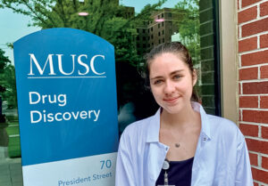 Camille Carthy '23 stands in front of a building with a sign that reads "MUSC Drug Discovery"