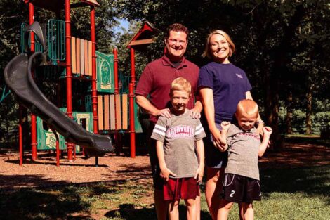 Lauren and Chris Anderson stand with their children with playground equipment behind them