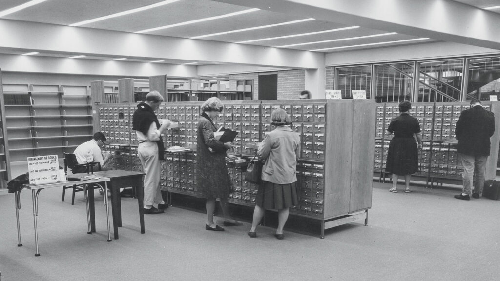 A black and white photo showing people using a card catalog in Skillman Library
